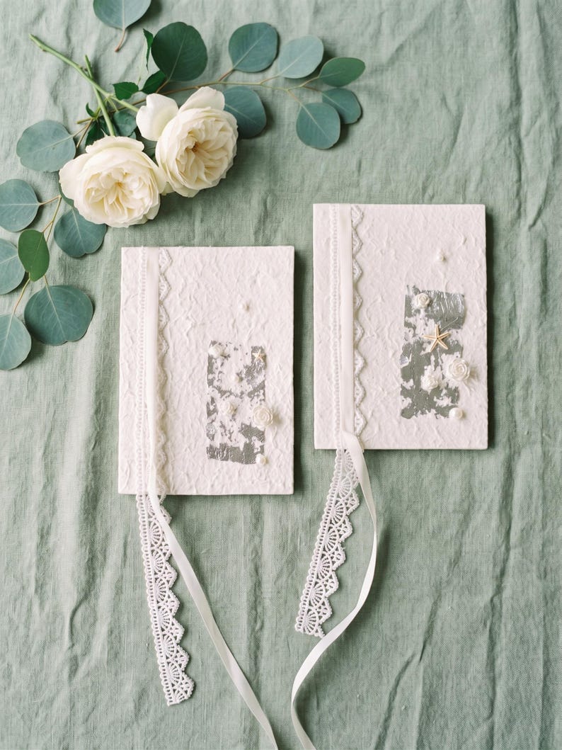 His and hers handmade paper vow books, flat lay with white flowers