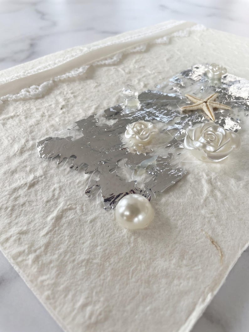 Close-up of silver leaf, pearl rose and starfish detail on vow book cover